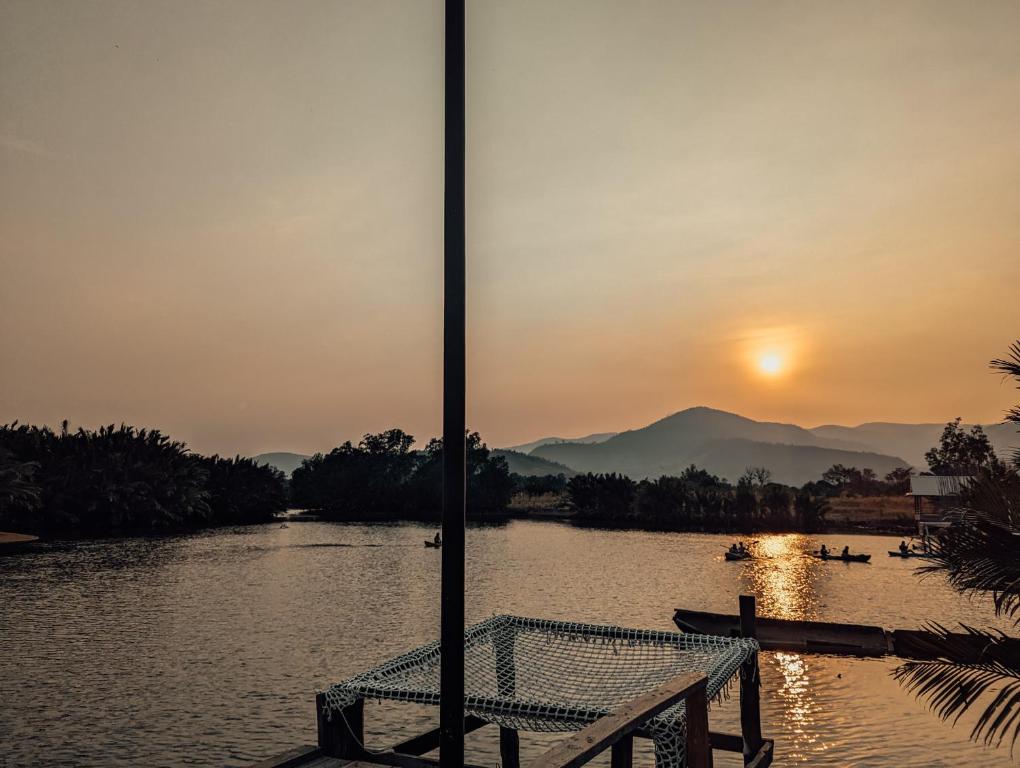 a bench sitting on the side of a river at sunset at Funky Moon Kampot in Kampot