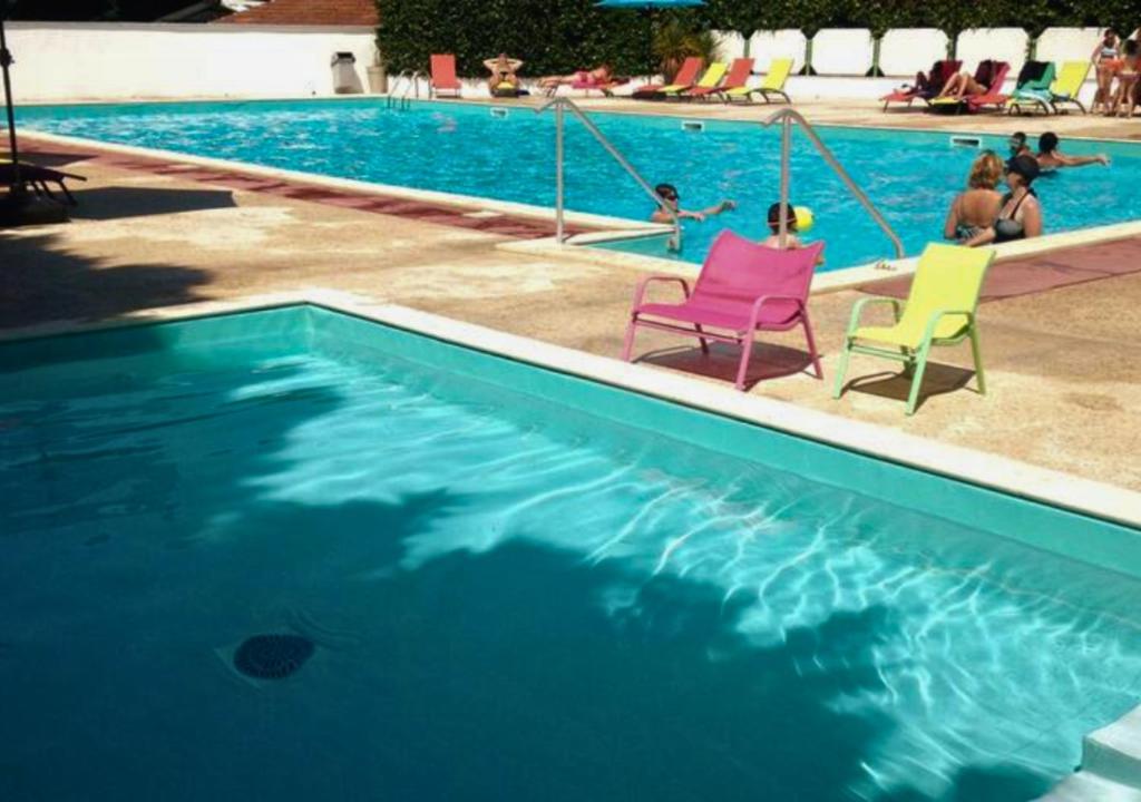 - une piscine avec 2 chaises et des personnes dans l'eau dans l'établissement Mobil-Home LA PALMYRE - Zoo, plage, animations, aux Mathes