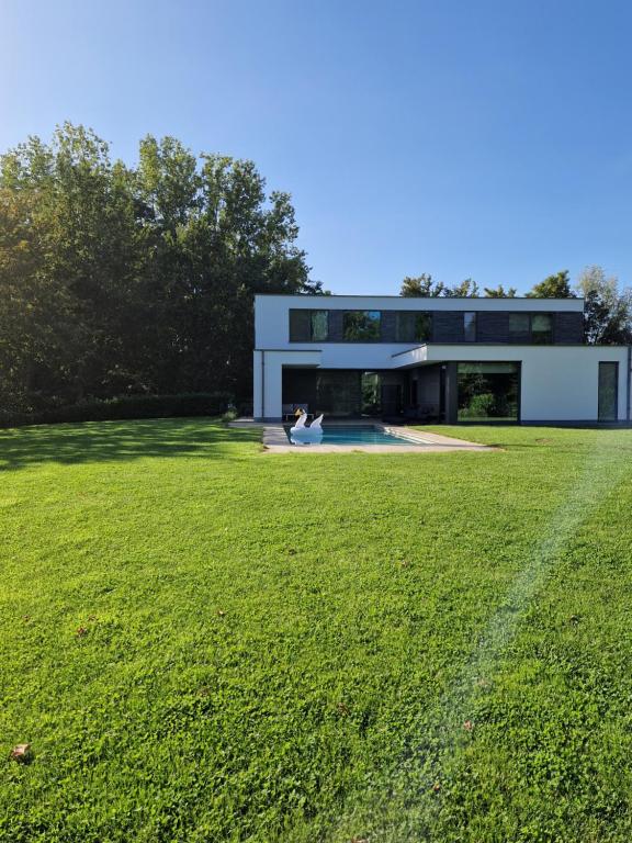 een modern huis met een groen veld ervoor bij Hele gezinswoning met zwembad te huur in Mechelen