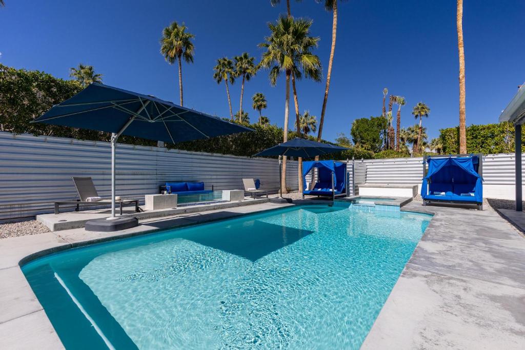 a swimming pool with two blue umbrellas and palm trees at Far Far Away in Vista Las Palmas in Palm Springs