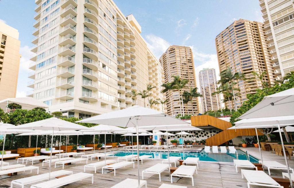 una piscina con sillas blancas, sombrillas y edificios en Hilton Vacation Club The Modern Honolulu, en Honolulu
