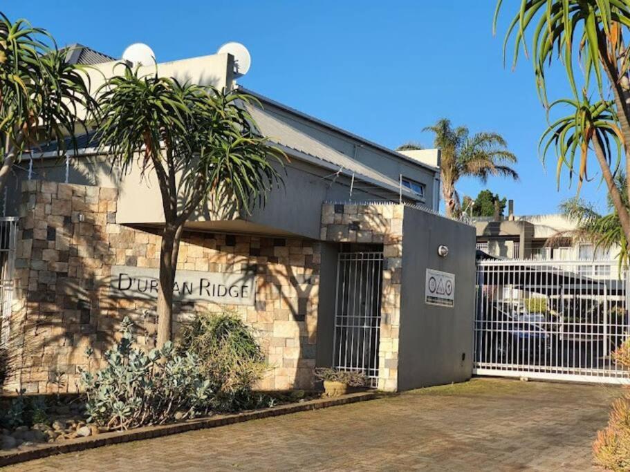 a building with a fence and palm trees in front of it at 1 Bedroom Apartment Tygervalley in Cape Town
