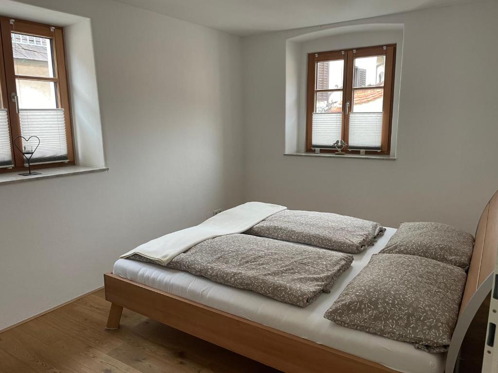 a bed in a white room with two windows at Altes Winzerhaus in der Wachau - neu renoviertes Haus mit Terrasse in Dürnstein