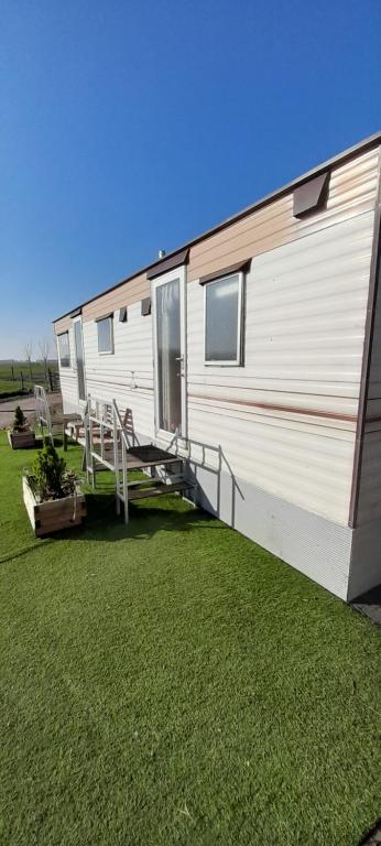 a white trailer with a porch and a grass yard at Stacaravan op de paardenboerderij Sneek in Sneek