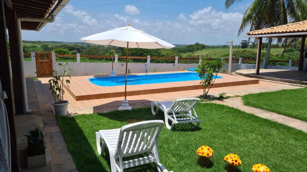 une cour avec deux chaises, un parasol et une piscine dans l'établissement HOTEL FAZENDA BOLANDEIRA, à Conde