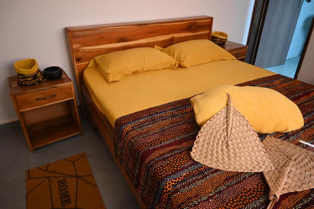 Bett mit einem Kopfteil aus Holz und einem Nachttisch in der Unterkunft Les Amazones Rouges Chambre Jaune in Ouidah