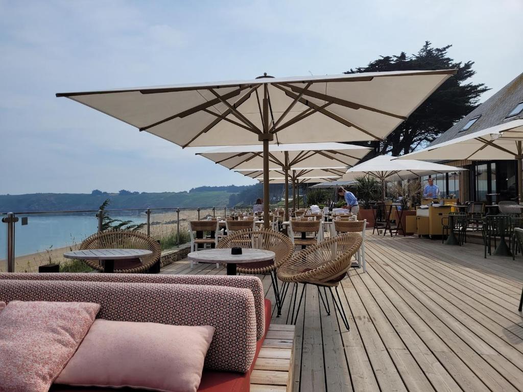 een houten terras met tafels, stoelen en parasols bij Mobilhome tout confort, proche Saint-Malo, à 50 m de la plage et du GR34 in Saint-Coulomb