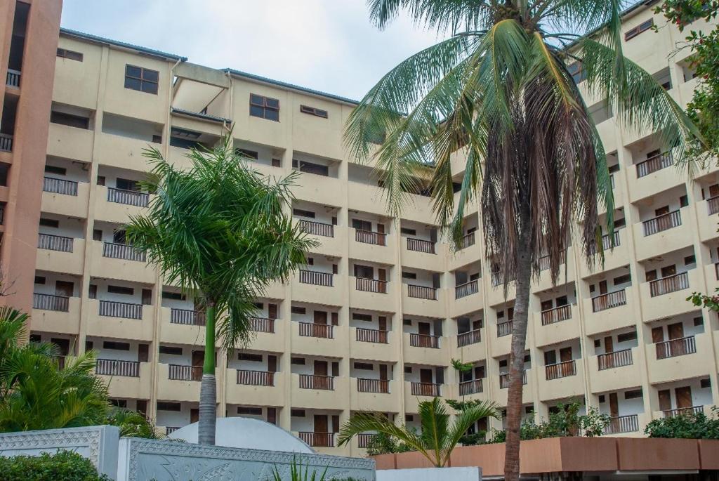 a large building with palm trees in front of it at Harmony Homes Beachfront in Diani Beach