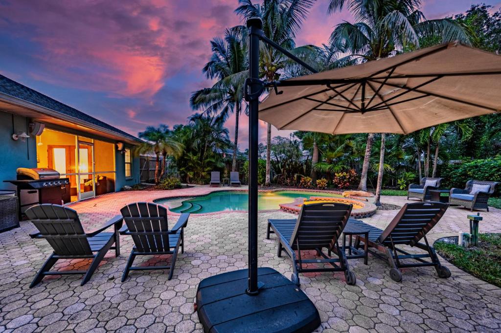 einen Tisch mit Stühlen und einen Sonnenschirm neben einem Pool in der Unterkunft Nautical Escape! Private pool home with a tropical backyard oasis! in Bradenton