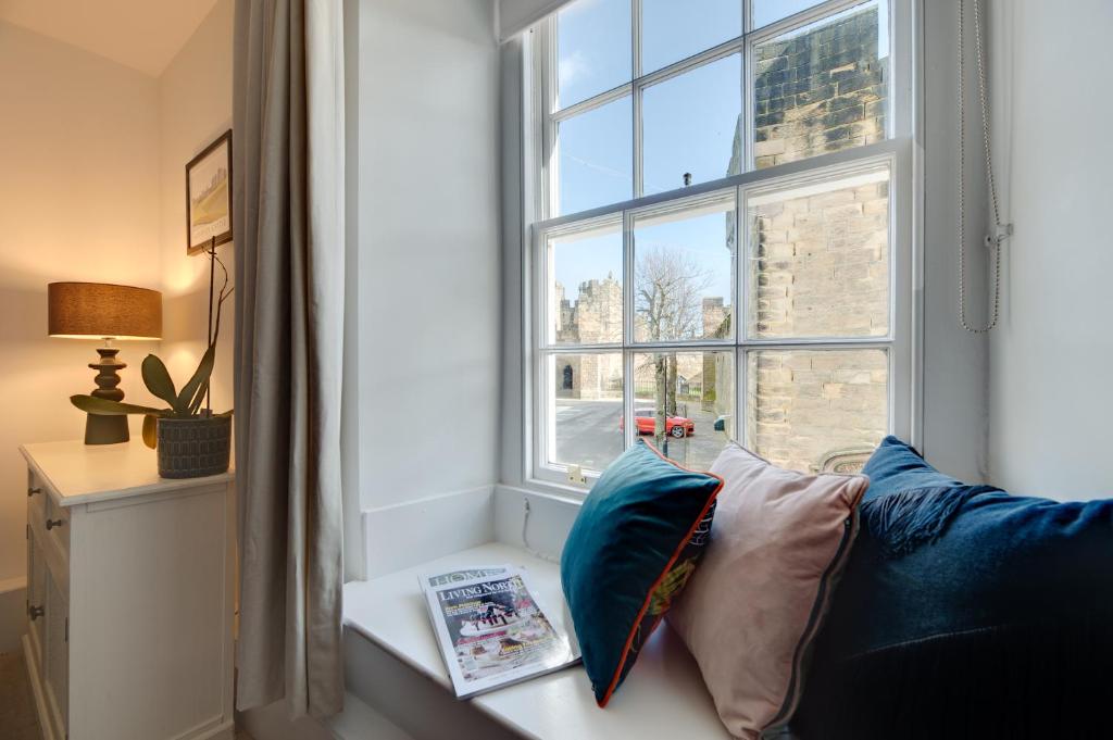 un siège près de la fenêtre avec un canapé bleu et un livre dans l'établissement Lionsgate View - luxury apartment opposite Alnwick Castle, à Alnwick