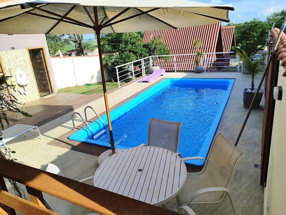 einen Pool mit einem Tisch und einem Sonnenschirm in der Unterkunft Linda Chacara com 2 Chalés em Boituva in Boituva
