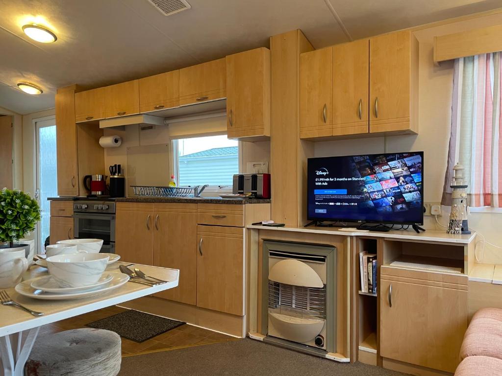 a kitchen with wooden cabinets and a flat screen tv at BelLa VistA - Holiday Home On The Beach in Clacton-on-Sea
