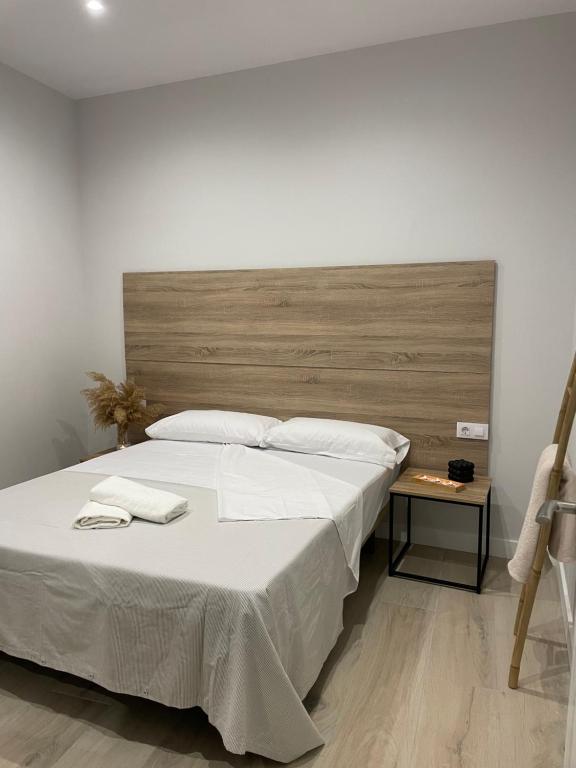 1 cama grande con sábanas blancas y cabecero de madera en Apartamentos Corredera 2, en Arcos de la Frontera