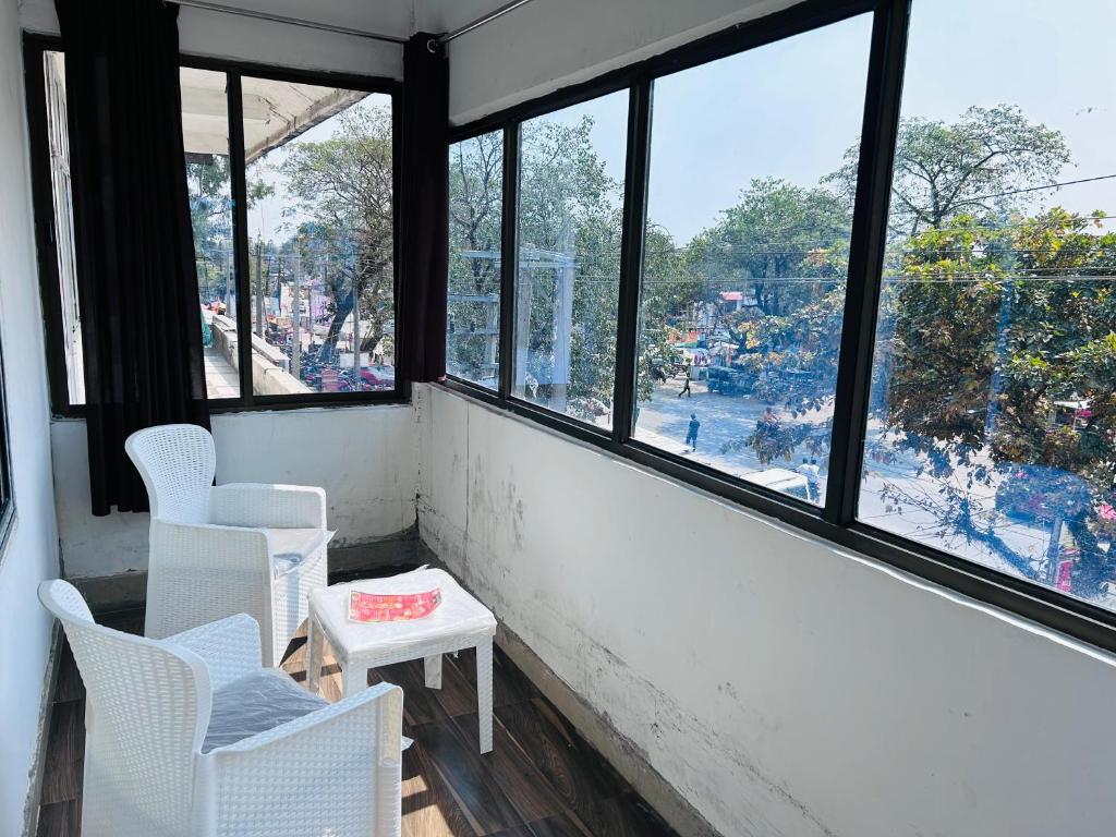 Habitación con sillas blancas y ventanas con vistas. en HOTEL CKD, en Gogāmukh