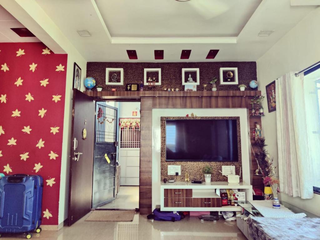 un salon avec une grande télévision à écran plat sur un mur rouge dans l'établissement 2BHK Flat Mid City Beed Bypass Sai Ashirward Apartment Aurangabad, à Aurangabad