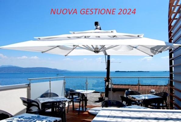 un patio con mesas y una gran sombrilla blanca en Happy Hotel Atelier Gardone Riviera Centro & Beach, en Gardone Riviera