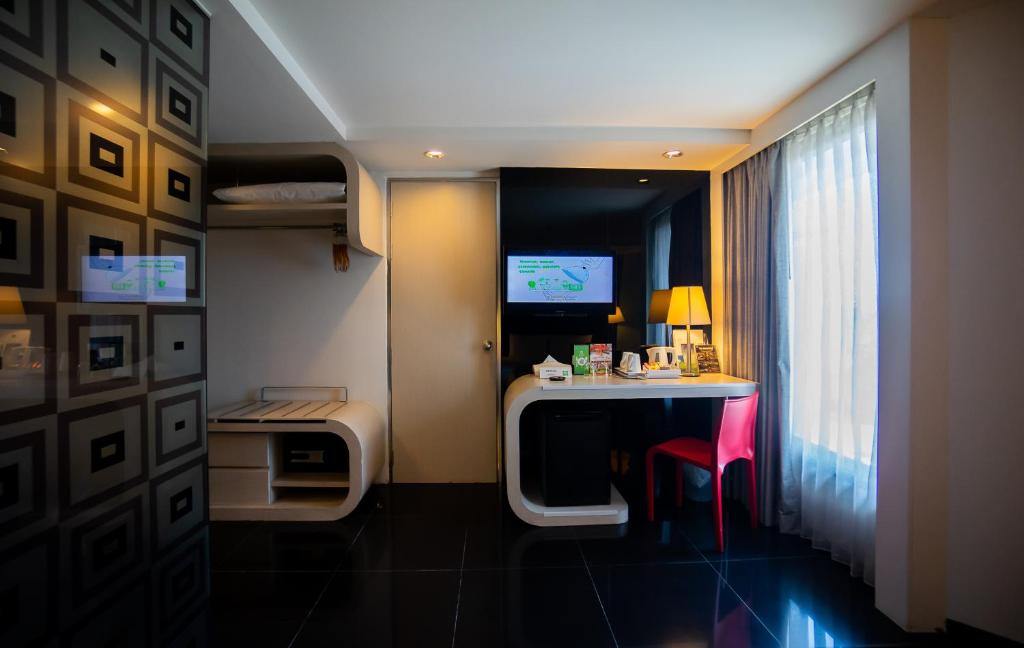 A modern hotel room with a small desk, television, wardrobe storage and a full-height curtained window.