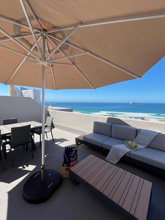 eine Terrasse mit Sofa und Sonnenschirm und Strand in der Unterkunft Coastal Hospitality - De Valle 65 in Mossel Bay