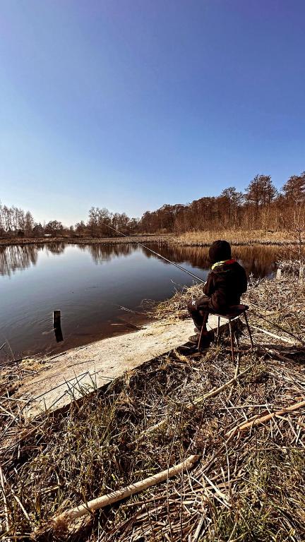 a person sitting on a chair next to a lake at Agro-Raj u Joli Charbrowo in Charbrowo