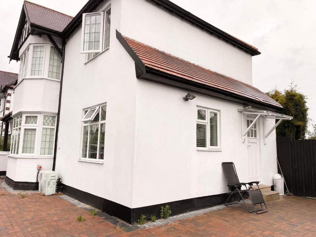 a white house with a black roof and a chair at Nice and Cosy One Bed Flat in Carshalton