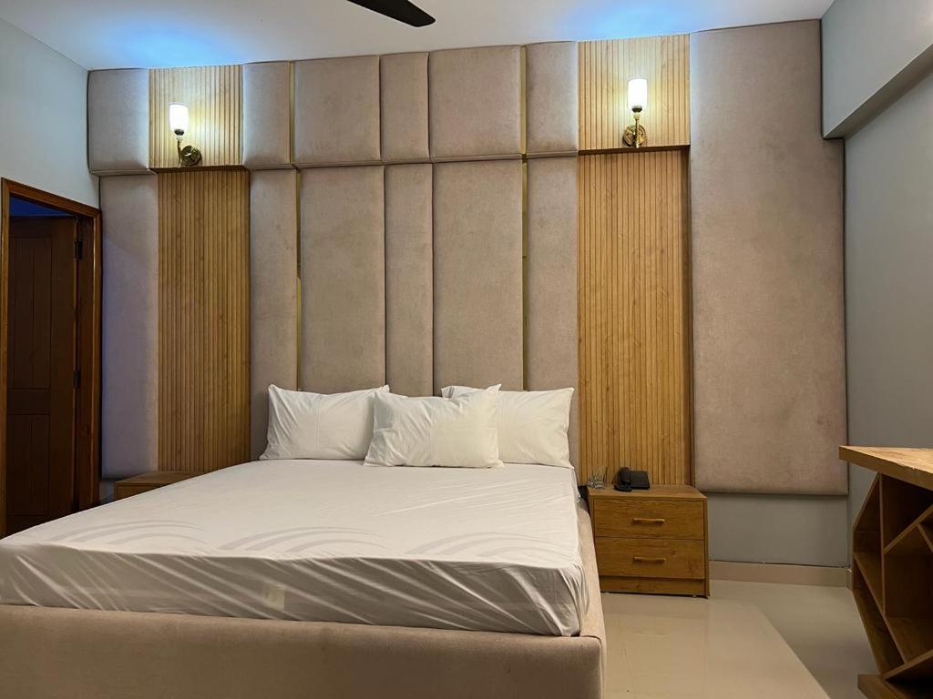 Schlafzimmer mit einem Bett mit weißer Bettwäsche und Kissen in der Unterkunft Marigold Accommodations in Karatschi