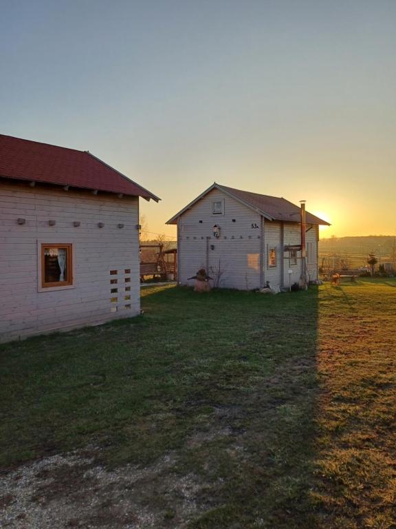 two buildings in a field with the sunset in the background at Magia Krutyni Domek nr2 in Ukta