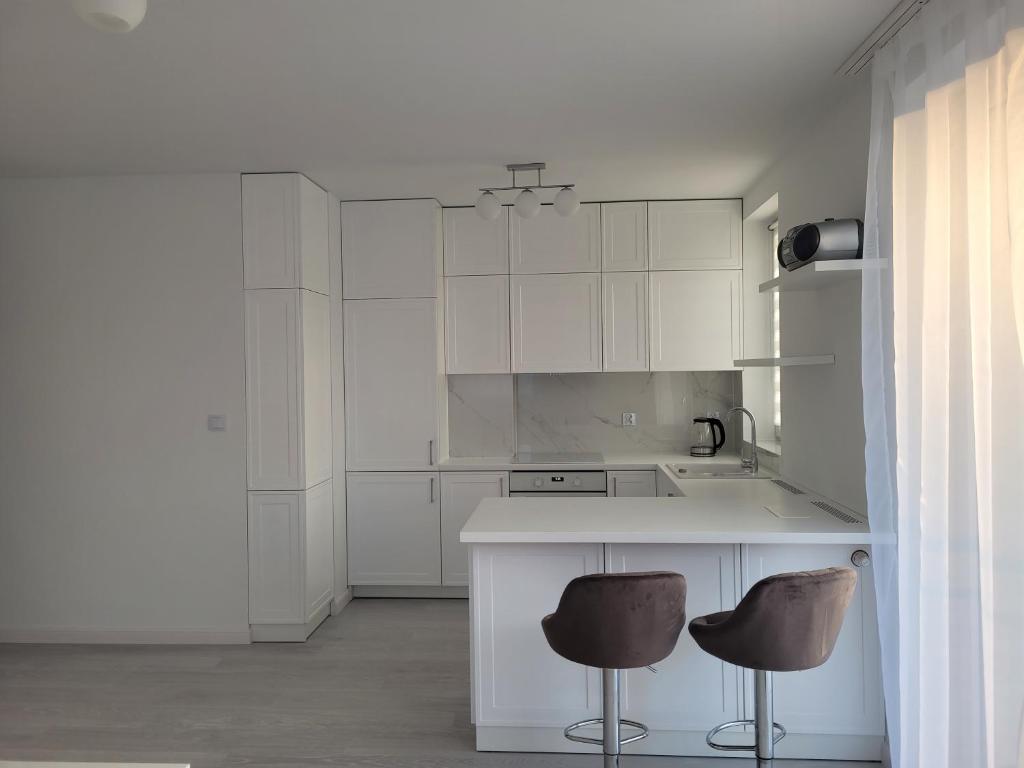 kuchnia z białymi szafkami i 2 stołkami barowymi w obiekcie Apartament Mistral w Krakowie