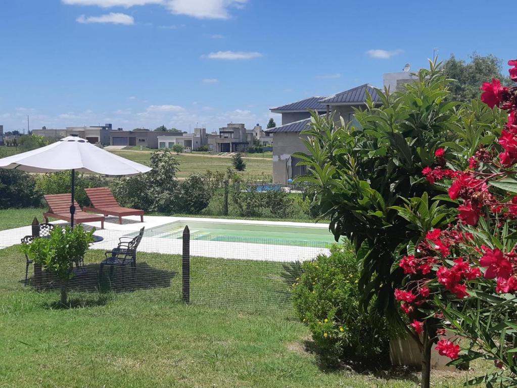 a pool with two chairs and an umbrella and flowers at Hermosa casa, calidad y tranquilidad garantizada in Concepción del Uruguay