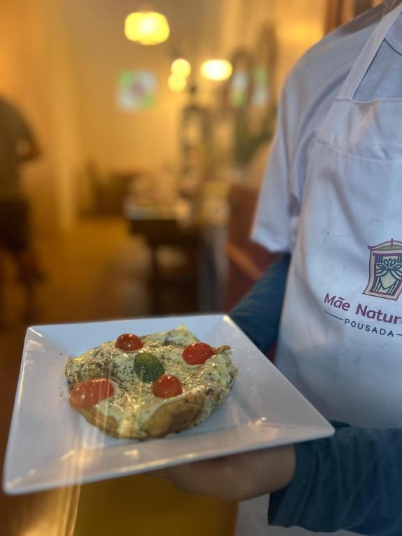 a person holding a plate with a pizza on it at Pousada Mãe Natureza in Pirenópolis