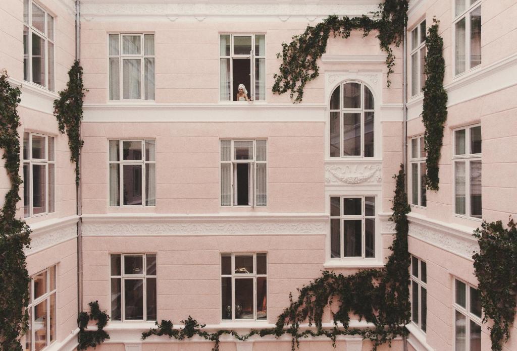 Eine Frau, die aus dem Fenster eines rosa Gebäudes schaut. in der Unterkunft Hotel Bella Grande in Kopenhagen