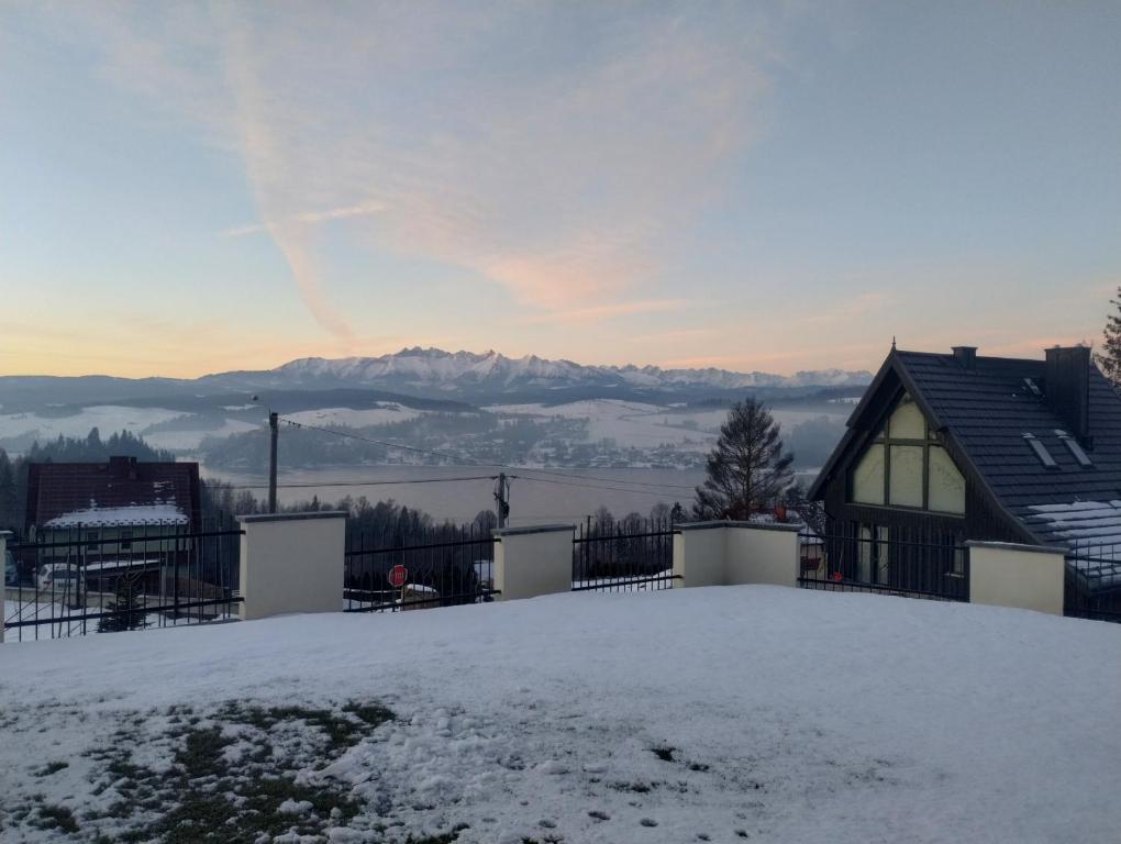 una casa cubierta de nieve con montañas en el fondo en Czorsztyn noclegi, en Czorsztyn