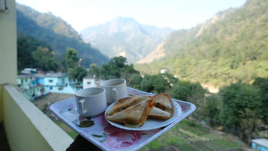 un plato con un sándwich y dos tazas en un balcón en Hotel Vardan - Ayur Stay, en Bijni