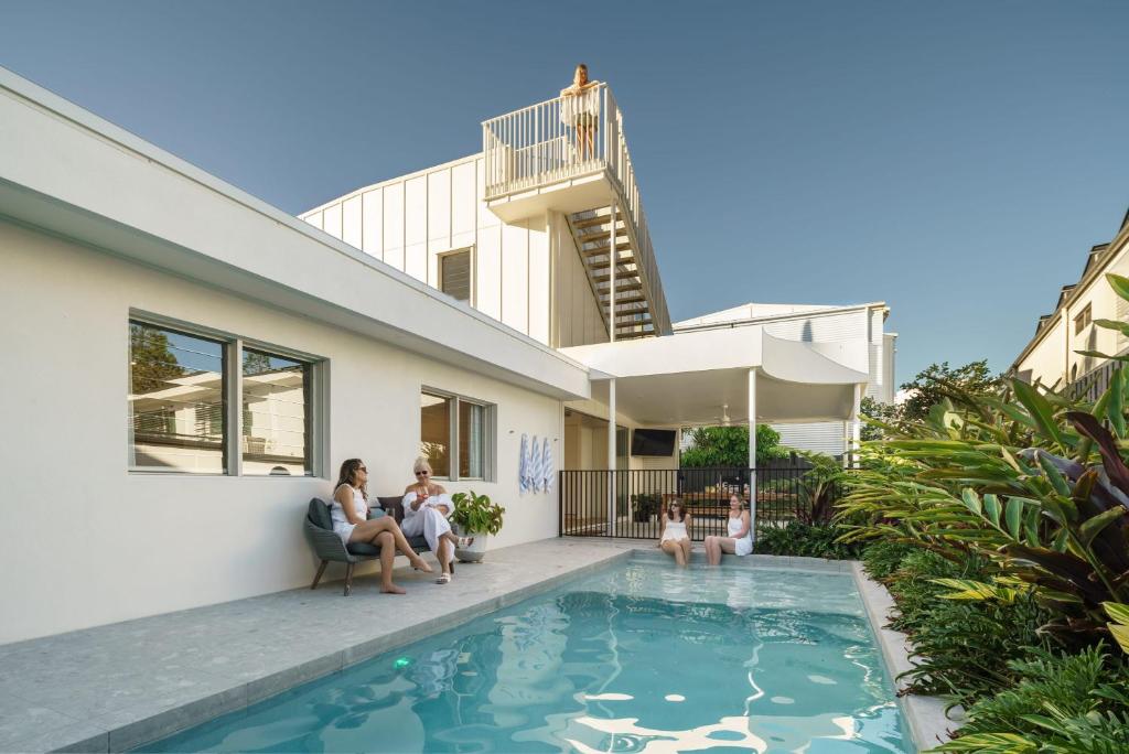 a group of people sitting around a swimming pool in front of a house at Villa Parkana - Beachside Buddina in Buddina