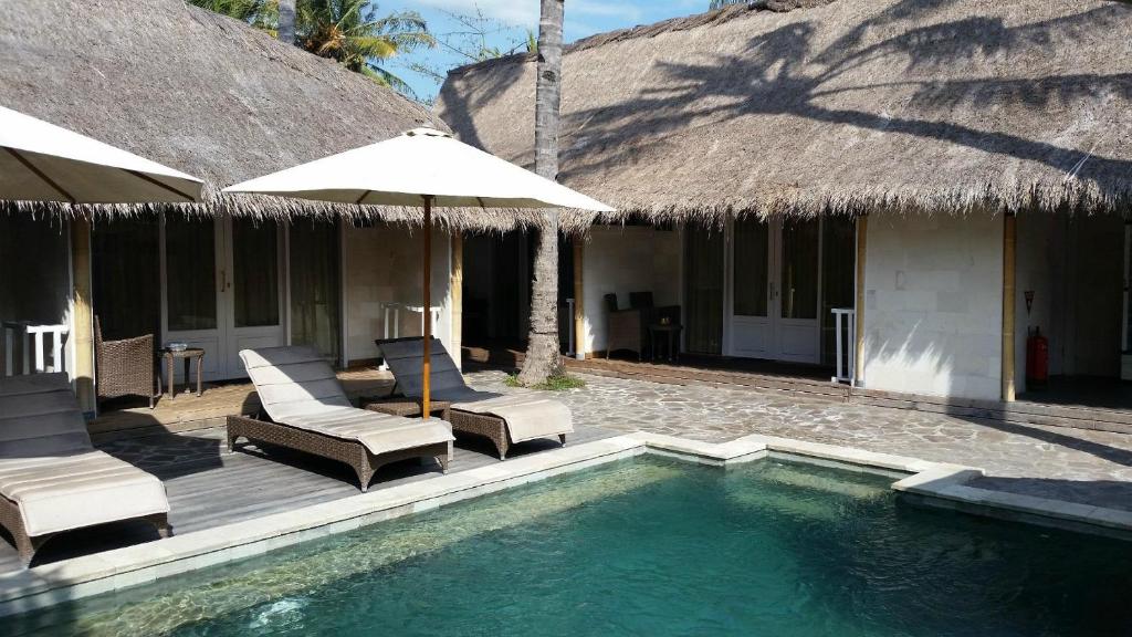 un complejo con piscina con sillas y sombrilla en Sol Villas Gili Air, en Gili Air