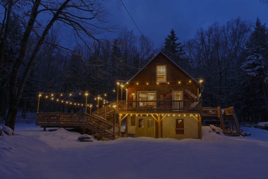 a house covered in lights in the snow at night at Dream Stratton Forest Cabin with Hot Tub and Fast WiFi in Stratton