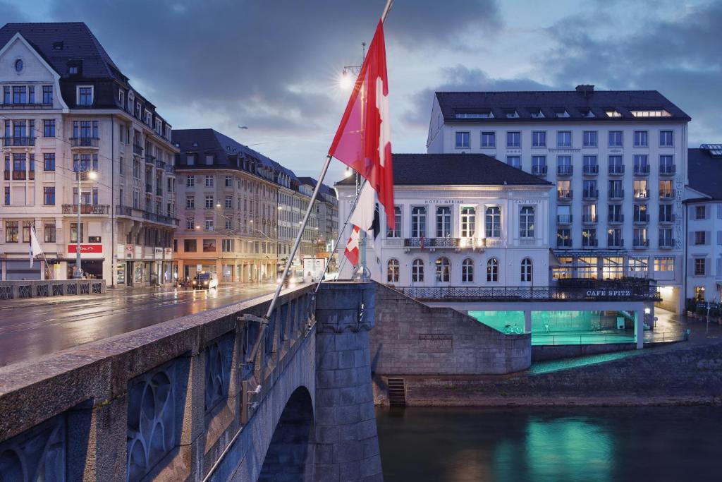 un puente sobre un río con dos banderas. en Merian Basel - Self Check-in, en Basilea