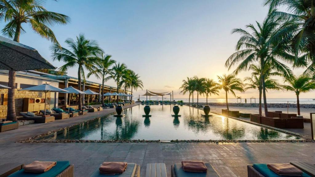 uma piscina de resort com palmeiras e uma praia em Mia Resort Nha Trang em Nha Trang