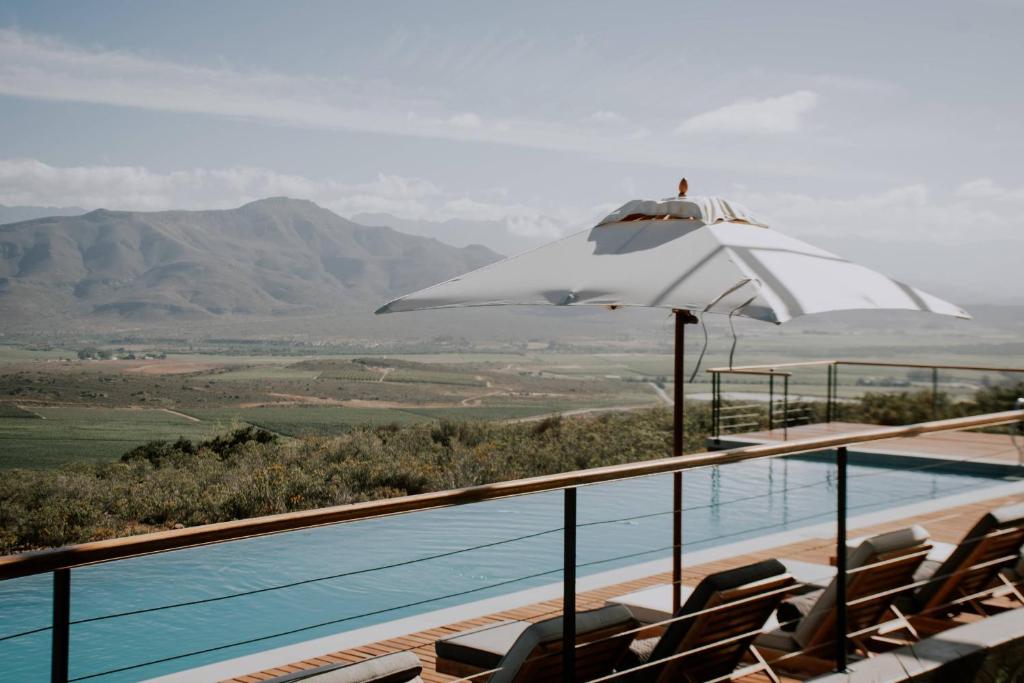 a swimming pool with a white umbrella and chairs at Khanyisa Mountain Lodge in Robertson