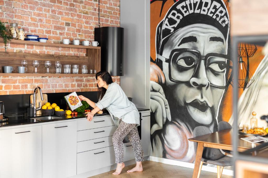 a woman standing in a kitchen next to a large painting at Lion Apartments - New Sopot by the sea! in Sopot