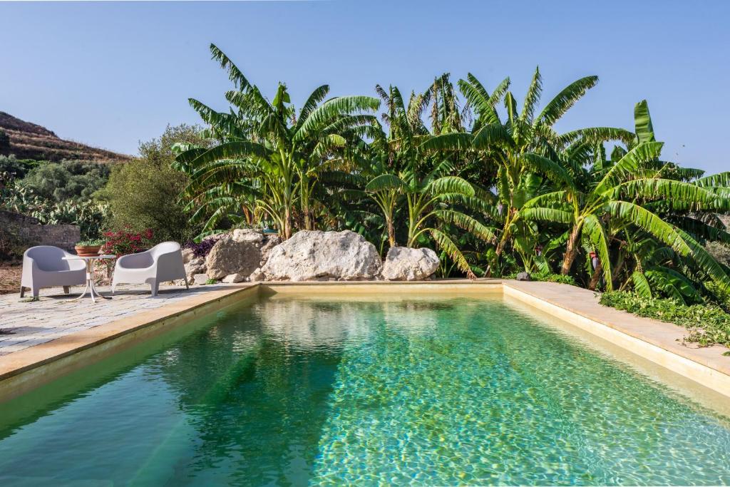 uma piscina com duas cadeiras e uma mesa e palmeiras em Villa Balatella con Piscina by Wonderful Italy em Augusta