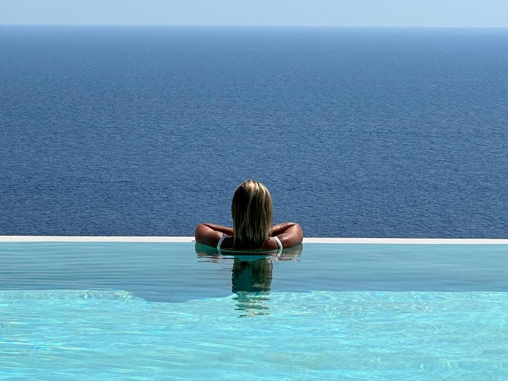 una mujer sentada en una piscina mirando el océano en Le Capase Resort Salento, en Santa Cesarea Terme