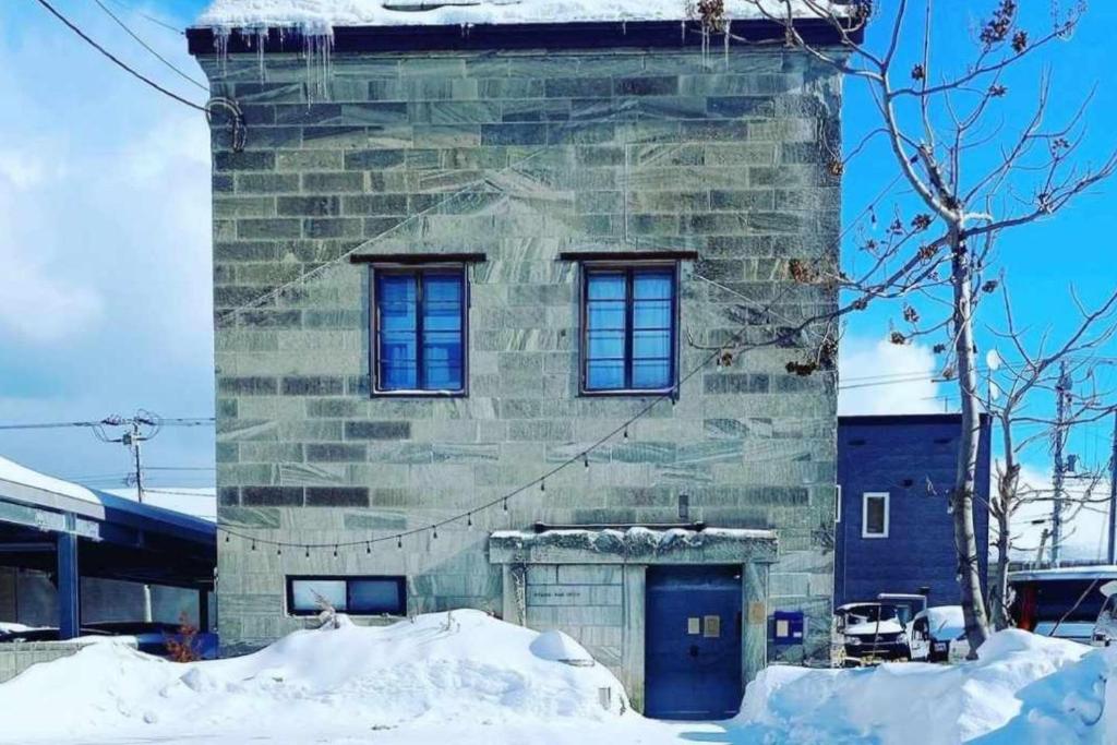 un edificio de piedra con 2 ventanas y una puerta azul en 石と鉄-House of STONE and IRON, en Otaru