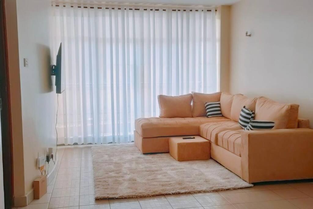 sala de estar con sofá marrón frente a una ventana en Premium 1 Bedroom Ruaka, en Ruaka