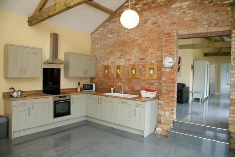 a kitchen with white cabinets and a brick wall at Owls Hoot at Tove Valley Cottages in Towcester