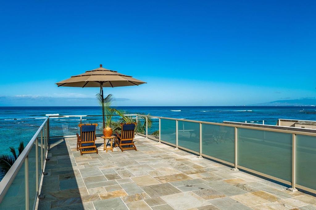 a balcony with two chairs and an umbrella and the ocean at Kove Villa in Honolulu