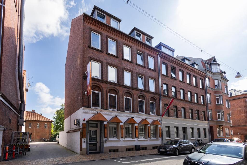 een groot bakstenen gebouw op een straat met auto's geparkeerd voor bij Milling Hotel Mini 19 in Odense