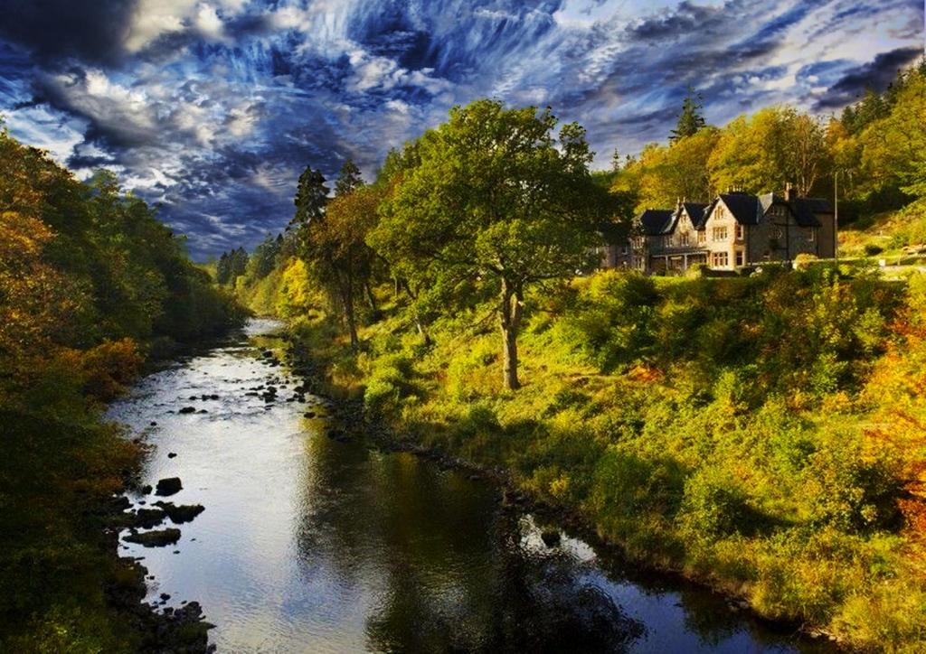 une rivière avec une maison au sommet d'une colline dans l'établissement Invergarry Hotel, à Invergarry