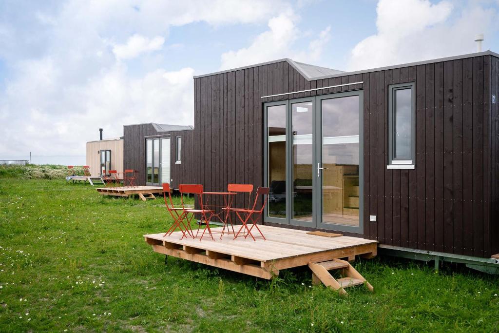 a small black house with red chairs on a deck at Tiny House Nature 7 Innenlage - Green Tiny Village Harlesiel in Carolinensiel