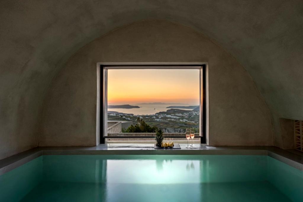 a bath tub with a view of the ocean from a window at Aethra Cave Suites in Pyrgos