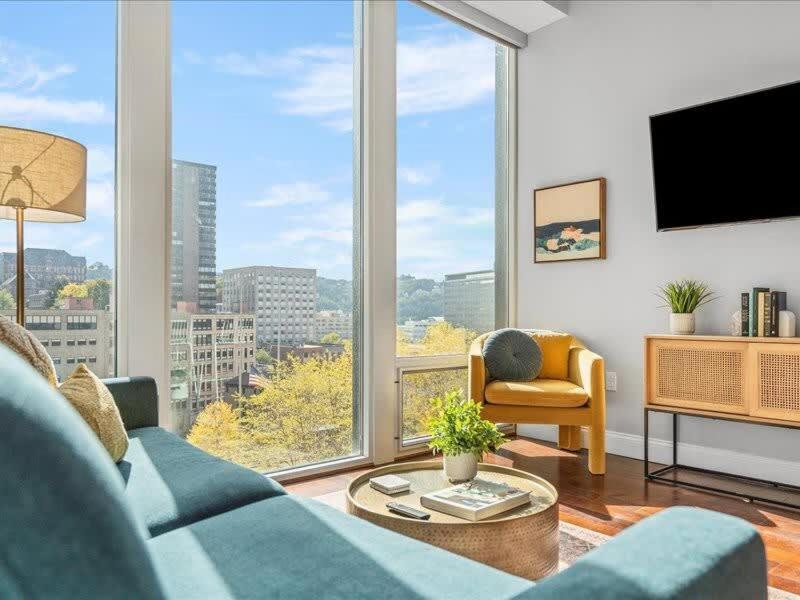 a living room with a blue couch and a large window at CozySuites Modern 1BR, PPG Paints Arena, Pitts in Pittsburgh